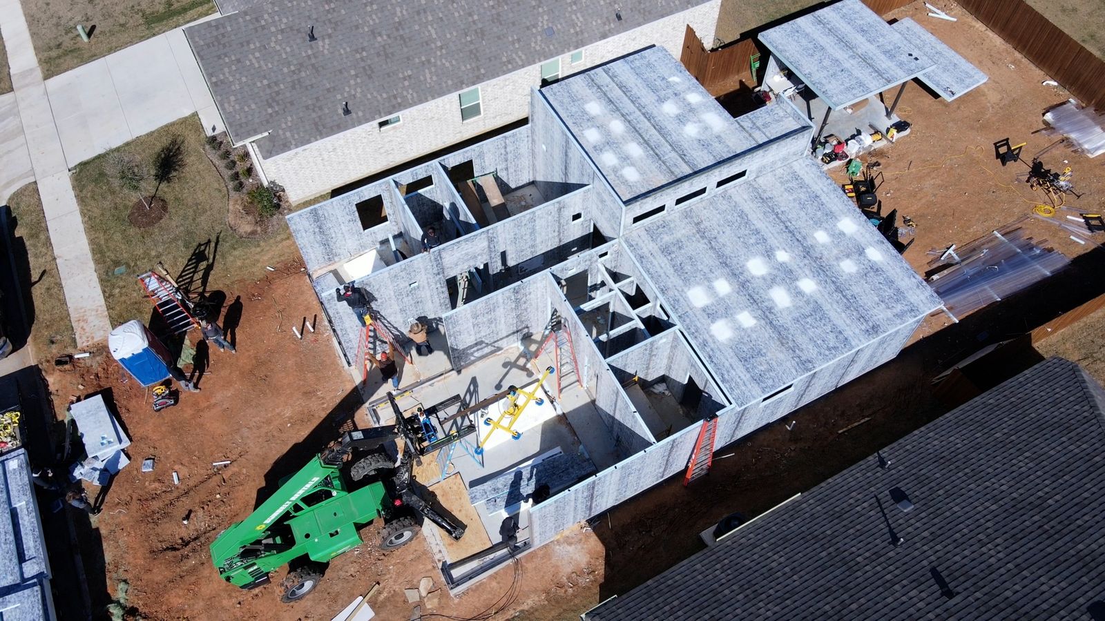 Aerial view of a modular shell with crane and crew on a residential lot