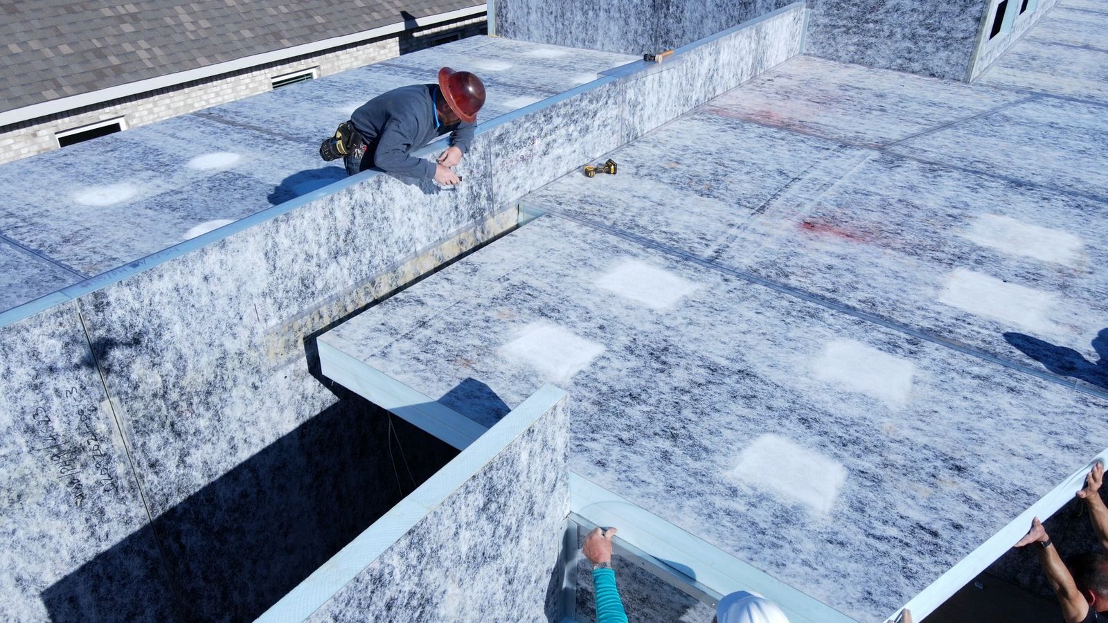 Workers fastening large roof panels across the top of a modular shell